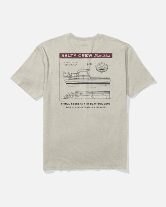 The Salty Crew Boat Shop Classic Tee - Bone features a blueprint-style boat graphic with SALTY CREW Boat Shop text, crafted from 100% soft spun cotton and highlighting details for skiffs, center consoles, and trawlers.