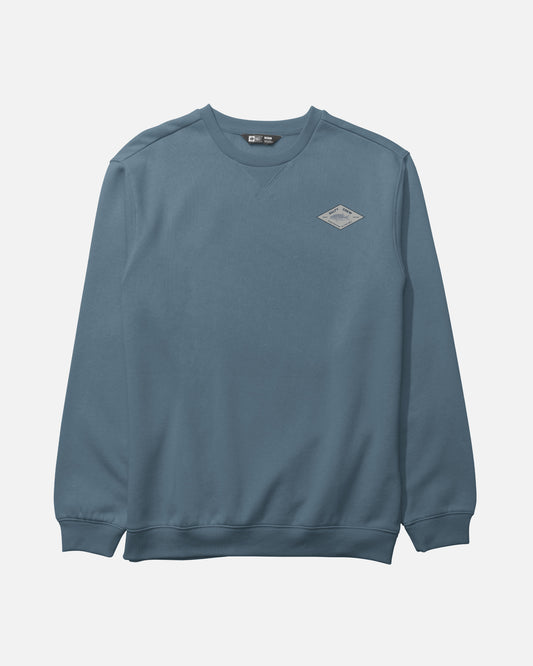 The Salty Crew Crafted Crew Fleece in Slate is a blue crewneck sweatshirt made from a cotton-polyester blend, featuring long sleeves with ribbed cuffs, a classic V-stitch gusset at the neckline, and a small diamond-shaped patch logo on the left chest, shown laid flat on a white background.