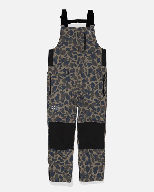 Salty Crew Long Range Tech Bib - Sand Camo features a camouflage pattern, black adjustable straps, black knee patches, side pockets, and logo patches on the chest and leg. Made from durable fabric and shown on a plain white background.