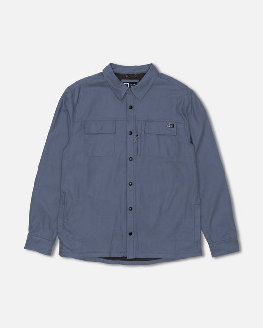 The Salty Crew Fathom Tech Shacket in Slate Grey is a long-sleeve, button-up shirt crafted from mid-weight twill for versatile wear. It features a classic collar, black buttons, and two chest pockets—one with a zipper detail—and is displayed on a plain white background.