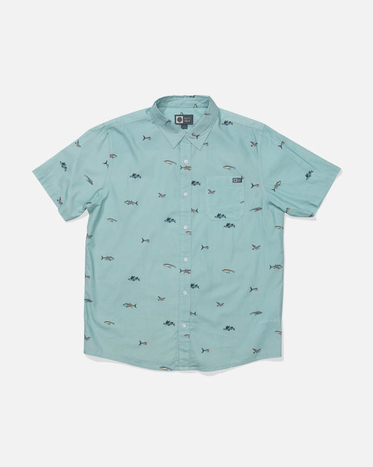 The Crew Button Up - Seaside is a light teal short-sleeve shirt made from mid-weight cotton blend, featuring a collar, branded resin buttons, small embroidered fish and shark patterns, and a left chest pocket with logo patch.