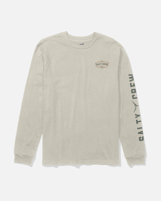The Salty Crew Tailfin Long Sleeve Tee in Bone is a beige, combed ringspun cotton t-shirt with “Salty Crew” text on the left chest and down the right sleeve, featuring a screenprinted small graphic patch on the chest.