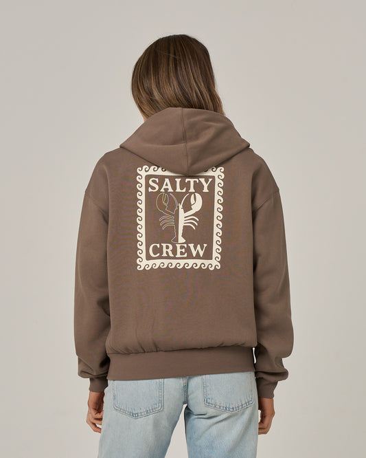A person wearing the Salty Crew Lobster Roll Hooded Zip in washed brown—a relaxed fit zip-front hoody featuring a lobster graphic on the back, crafted from soft cotton-polyester fleece—paired with light blue jeans and standing against a plain background.