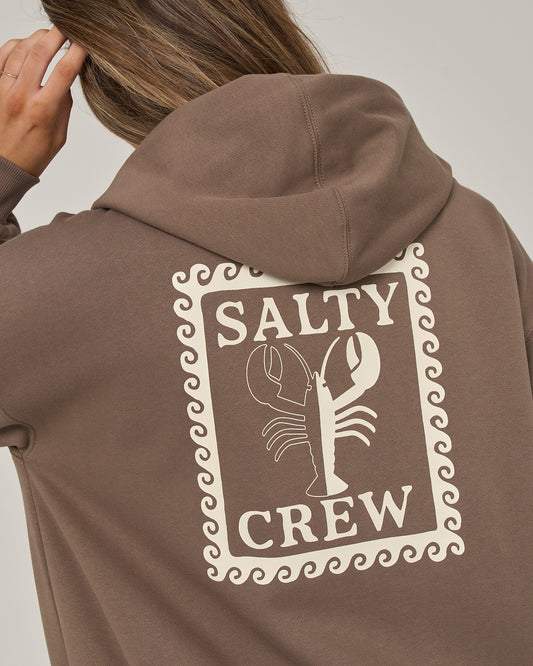 A person wearing the Salty Crew Lobster Roll Hooded Zip in washed brown—a relaxed fit cotton polyester fleece hoodie featuring a lobster graphic and “Salty Crew” text on the back outlined by a wavy border—touches their head.