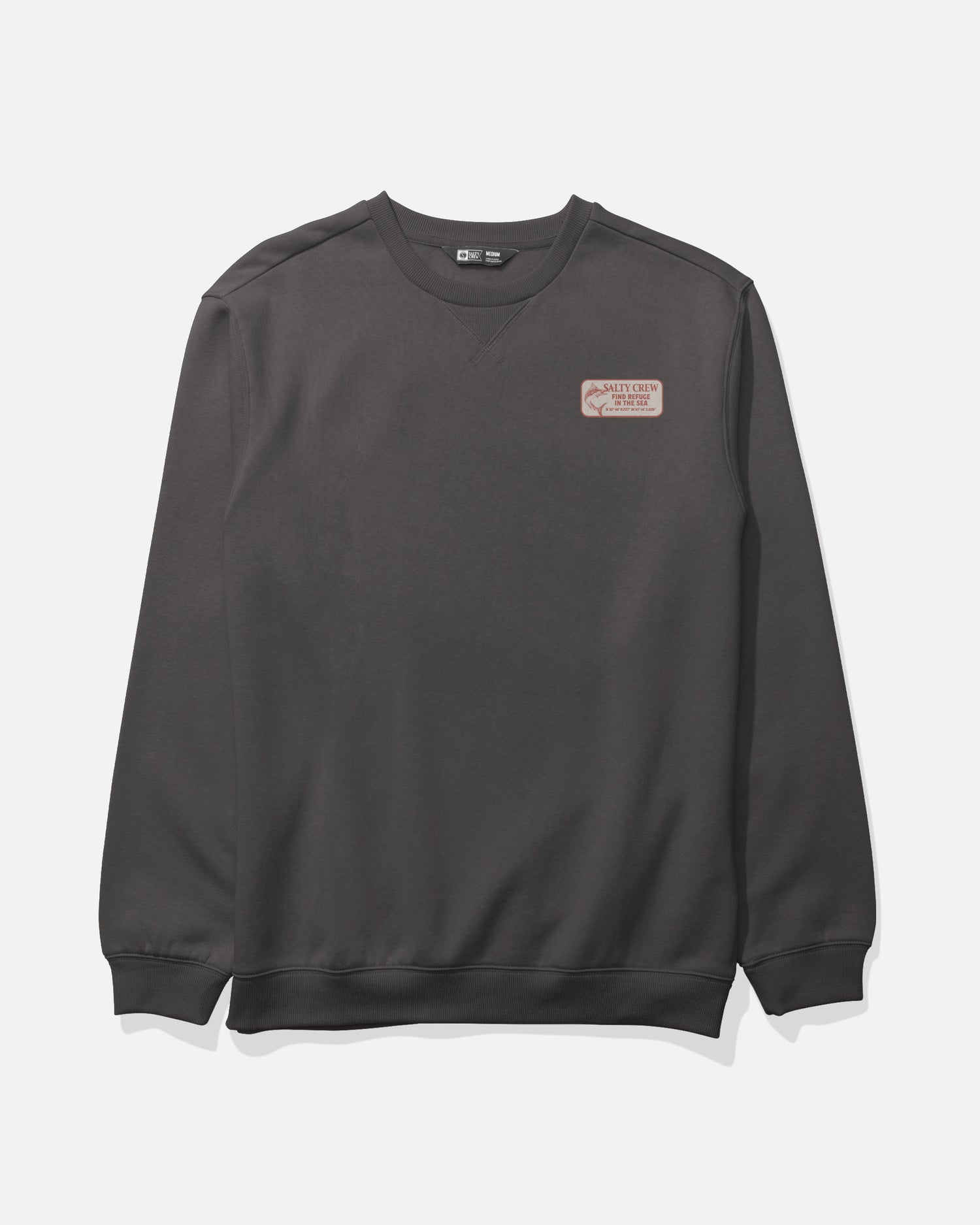 A Salty Crew Crafted Crew Fleece in dark grey, made from mid-weight cotton polyester, featuring a crewneck with a subtle V-stitch gusset at the neckline and a small rectangular patch with text and graphic on the left chest, is laid flat on a white background.