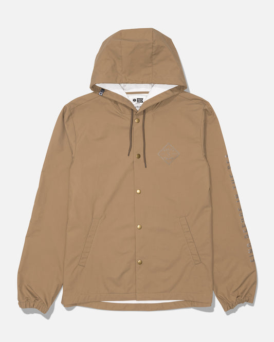 The Tippet Snap Jacket by Salty Crew in washed brown features a durable nylon shell, front snap buttons, two angled pockets, elastic cuffs, and black drawstrings. A small Salty Crew logo is screenprinted on the left chest, with text detailing running down the left sleeve.