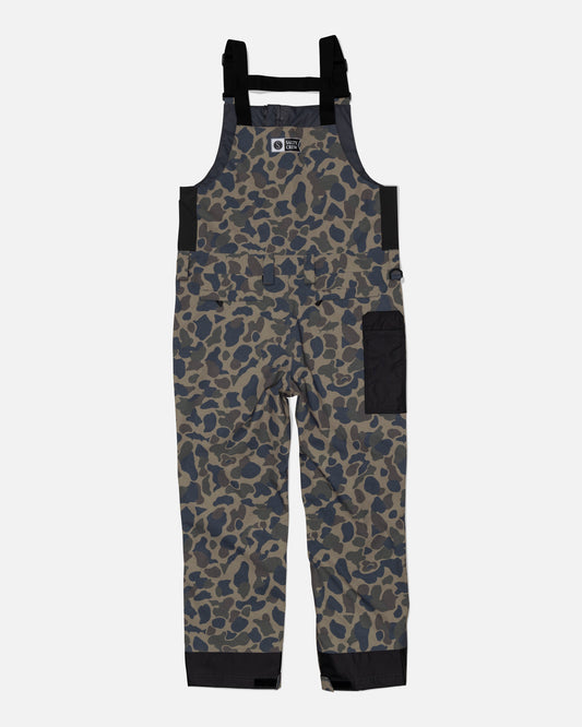 The Salty Crew Long Range Tech Bib - Sand Camo features black adjustable straps, a chest pocket flap, a large side pocket, reinforced black ankle panels, and a front zipper for durability and long-lasting performance.