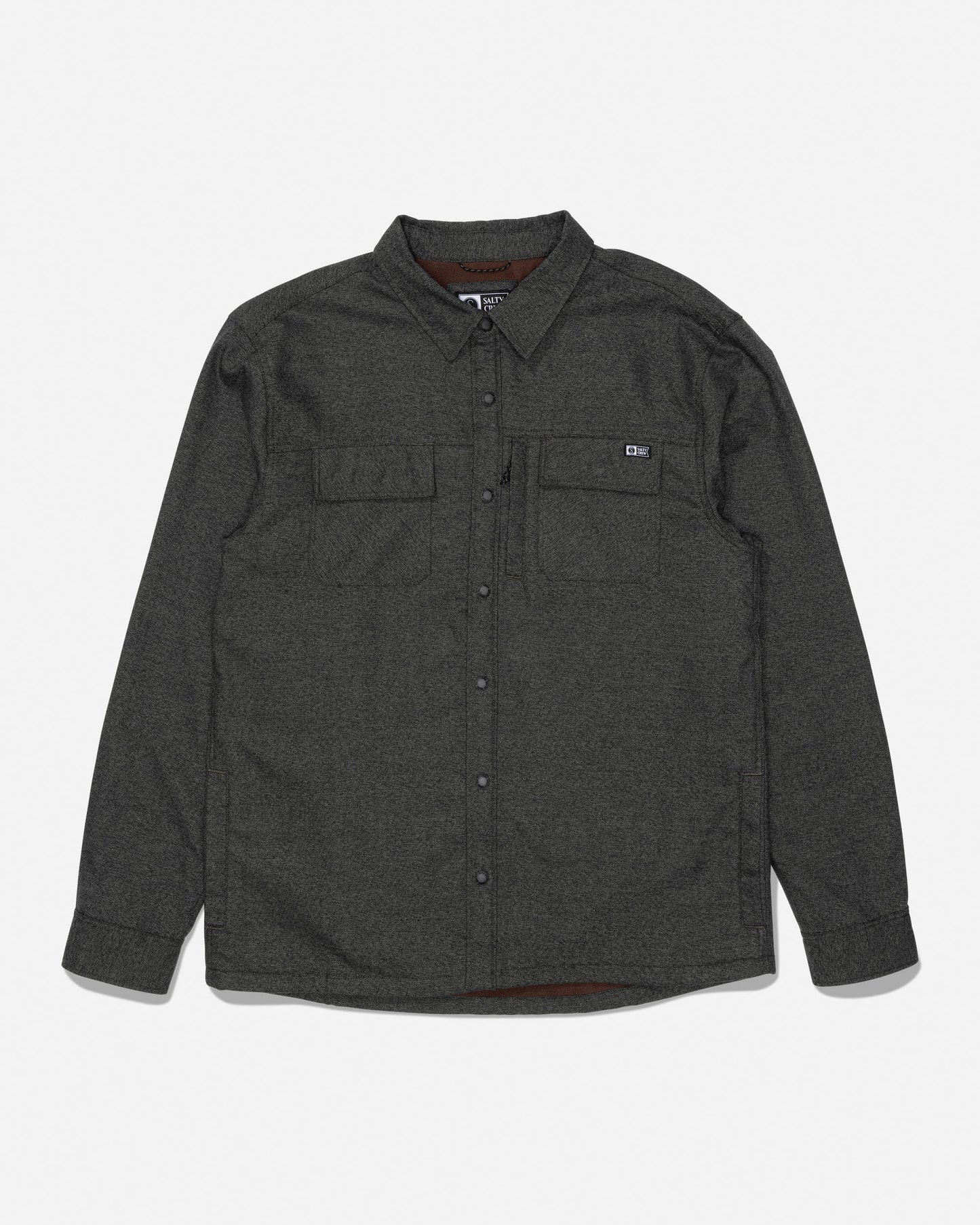 The Salty Crew Fathom Tech Shacket in Agave is a long-sleeve, dark gray button-up shirt made from mid-weight twill, featuring two chest pockets—one accented with a small rectangular logo patch. The shirt is displayed flat against a white background.