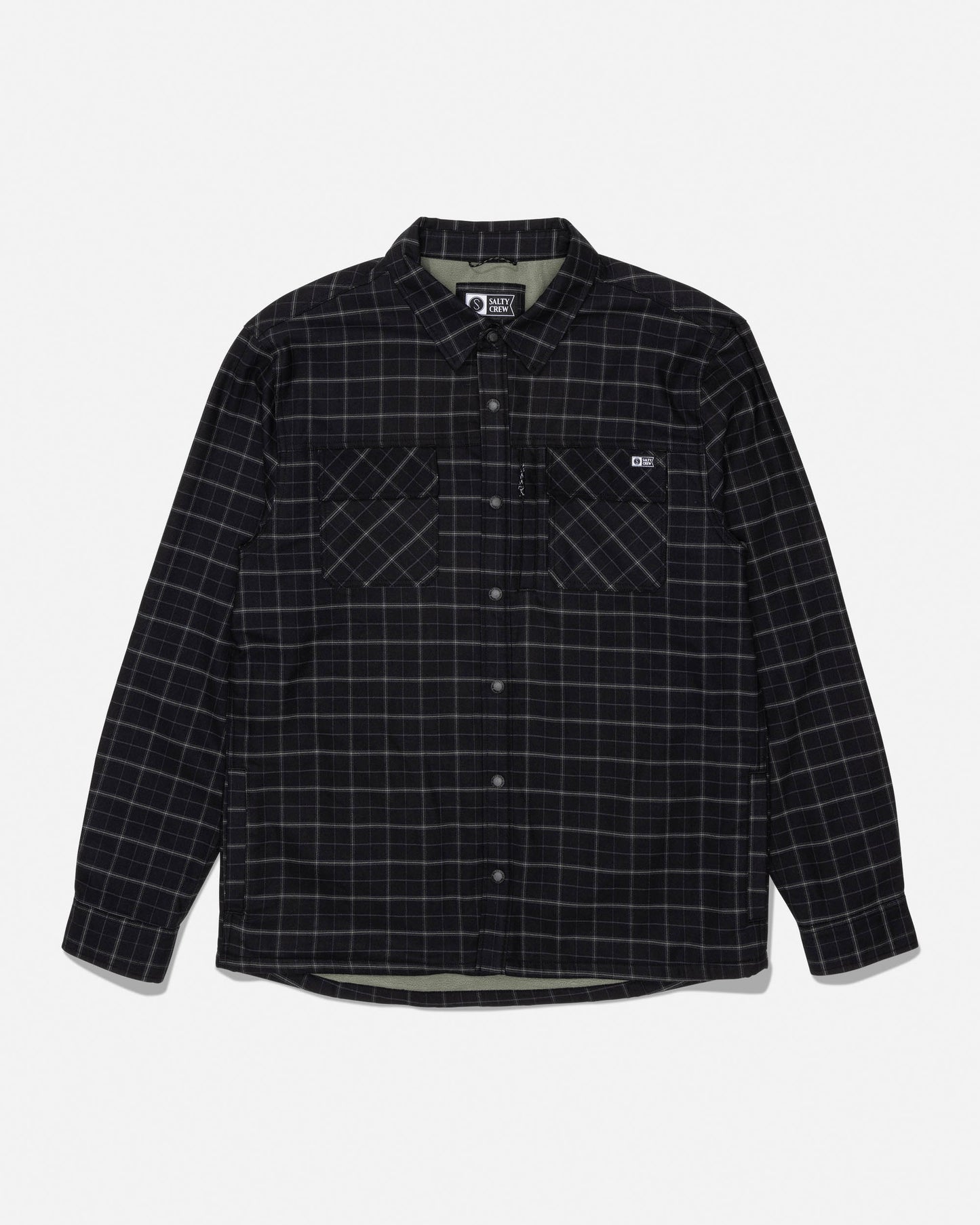 The Salty Crew Fathom Tech Shacket in Black/Green features long sleeves, a button-up front, a white grid pattern over black mid-weight twill fabric, dual chest pockets, and a small logo on the left pocket. The shirt is displayed laid flat on a white background.