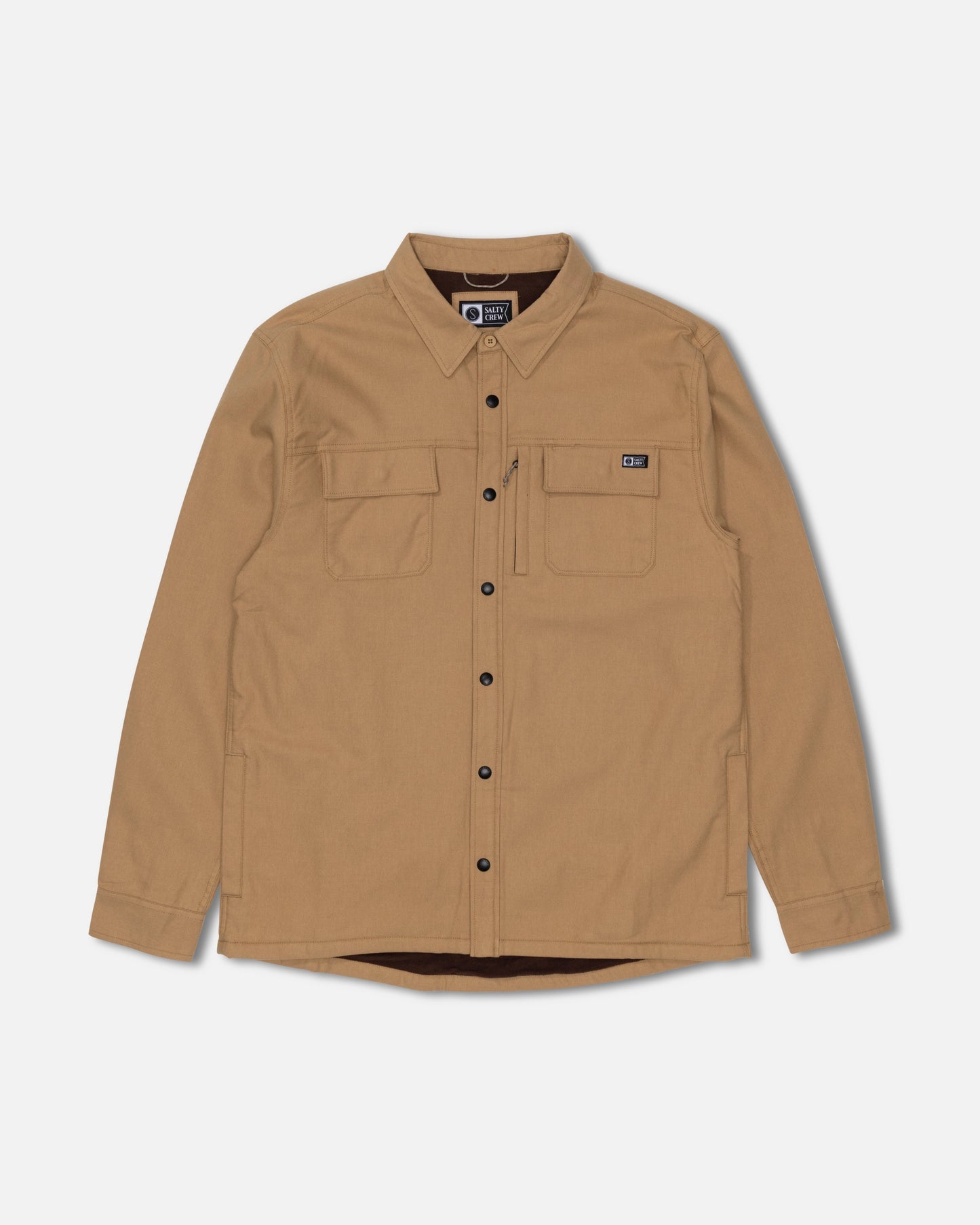 The Salty Crew Fathom Tech Shacket in Khaki features long sleeves, two chest pockets with a small black patch on the left pocket, and black buttons. Crafted from comfortable mid-weight twill for lasting durability, it’s shown here against a plain white background.