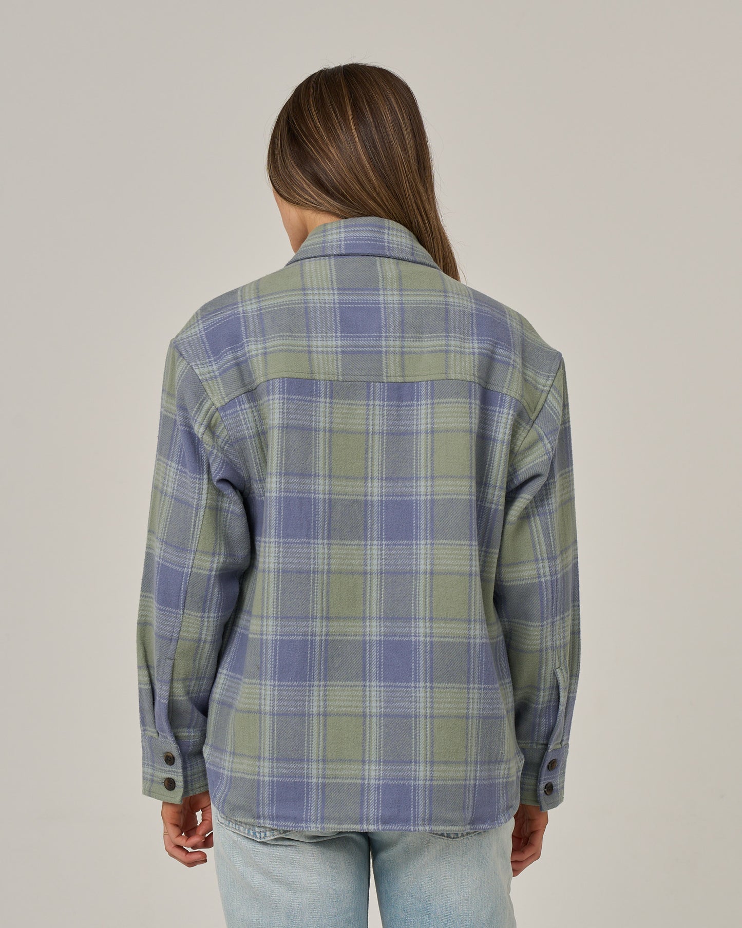 A person with long brown hair, wearing the Salty Crew Day Trip Shacket - Flint made from heavyweight cotton blanket flannel and light blue jeans, is standing facing away from the camera against a plain light background.