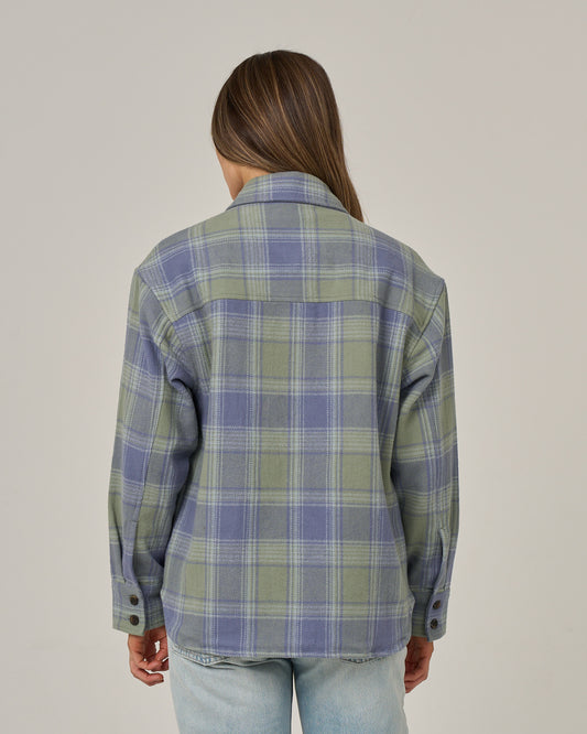 A person with long brown hair, wearing the Salty Crew Day Trip Shacket - Flint made from heavyweight cotton blanket flannel and light blue jeans, is standing facing away from the camera against a plain light background.