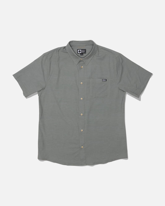 Introducing the Salty Crew Drifter UV Button Up in Agave—a short-sleeve, light gray shirt featuring a collared neckline and a left chest pocket accented with a small rectangular logo tag above it. Made from quick-dry fabric and offering UPF 50+ sun protection, this shirt ensures comfort and safety during sunny days.