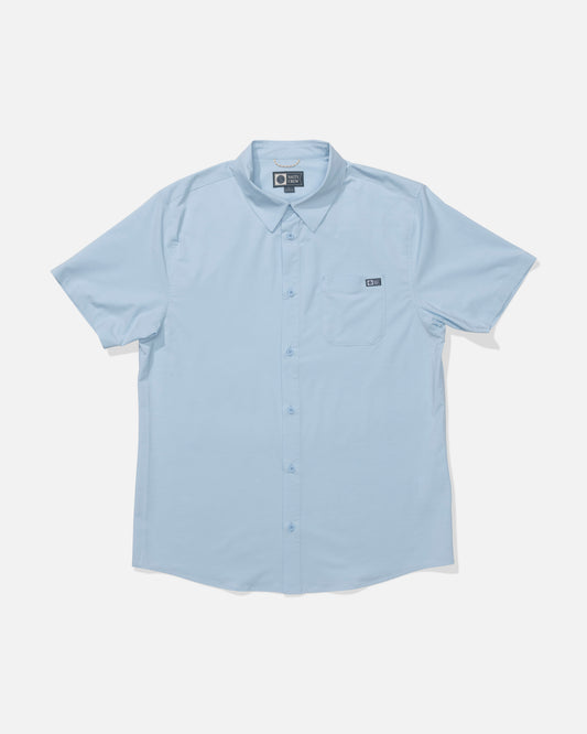 The Salty Crew Drifter UV Button Up in Clear Sky is a light blue, short-sleeve collared shirt with a left chest pocket. Made from moisture-wicking, quick-dry fabric for all-day comfort. Displayed on a white background.