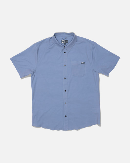 The Salty Crew Drifter UV Button Up in Hitch Blue is a light blue short-sleeve shirt featuring dark buttons and a left chest front pocket. Designed for all-day comfort with quick dry performance, it’s shown laid flat on a white background.
