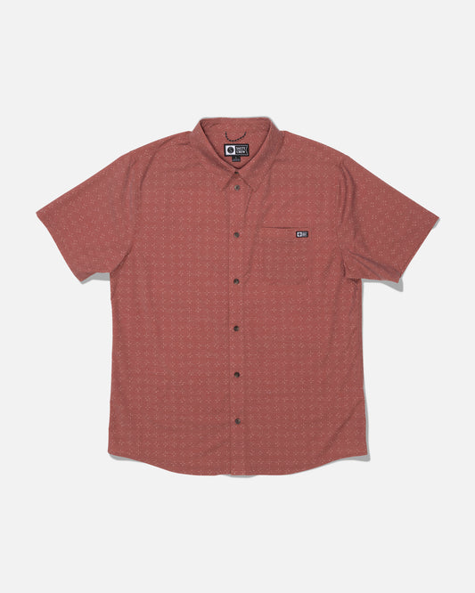 The Salty Crew Drifter UV Button Up in Mid Red is a short-sleeve, button-up shirt featuring a subtle dotted pattern, front chest pocket with a small logo patch, and crafted from moisture-wicking fabric with UPF 50+ sun protection. The shirt is laid flat on a white background.