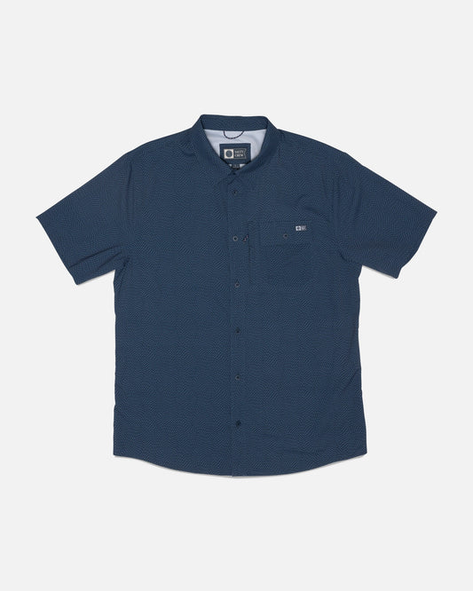 The Salty Crew Flagship UV Button Up in Mid Blue is a short-sleeve shirt featuring a subtle dotted pattern, a single chest pocket with a small logo tag nearby, and is crafted from quick-dry fabric for added comfort. The shirt is displayed laid flat on a white background.