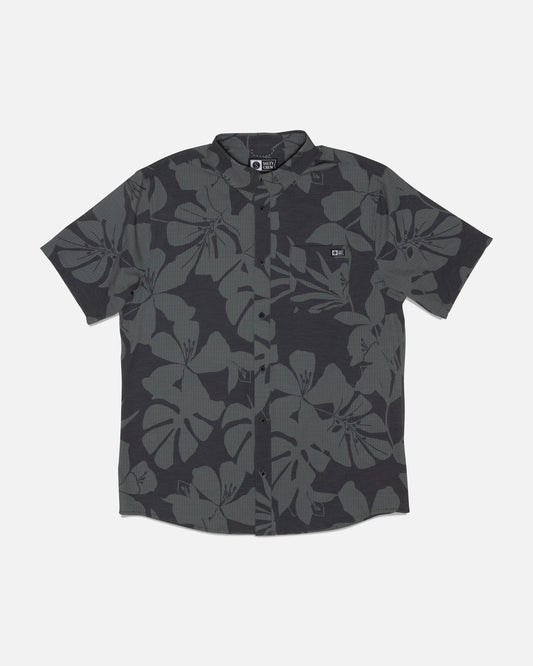 The Salty Crew Breezer Perforated Button Up in Black/Green is a short-sleeve shirt featuring a black and dark gray tropical leaf pattern, crafted from lightweight, breathable fabric with UPF 50+ sun protection, shown laid flat on a white background.