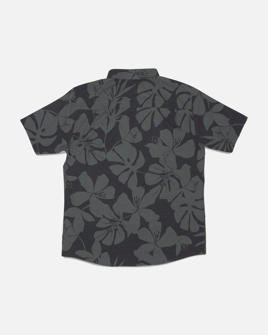 The Salty Crew Breezer Perforated Button Up - Black/Green features a short-sleeve design with a dark gray floral Hawaiian pattern on a black background, shown laid flat with the back facing up. Made from lightweight, breathable fabric for enhanced comfort.