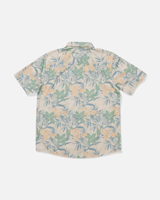 The Crew Button Up - Off White is a short-sleeved, mid-weight cotton blend shirt featuring a pale background with green leaves and yellow flowers, shown flat with the back side up. A woven label detail completes the look.