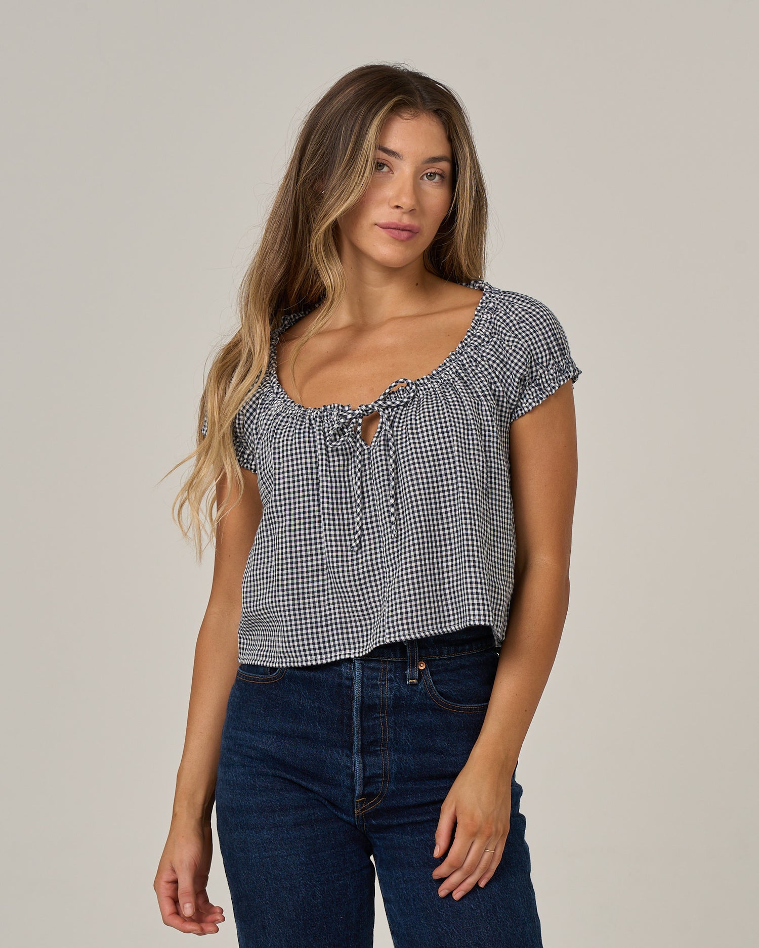 A woman with long, wavy hair wears the Salty Crew “Fresh Catch - True Navy” top with short sleeves, styled with blue jeans and standing against a plain light background.