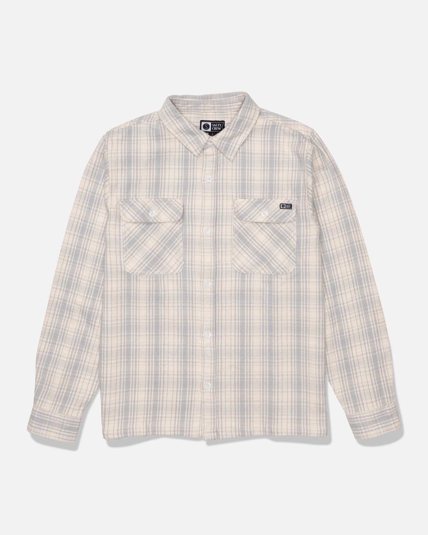 The Salty Crew Windward Flannel in Off White is a beige and light gray plaid button-up shirt, crafted from heavyweight cotton twill with a garment wash finish. It features two chest pockets and long sleeves, and is displayed on a white background.