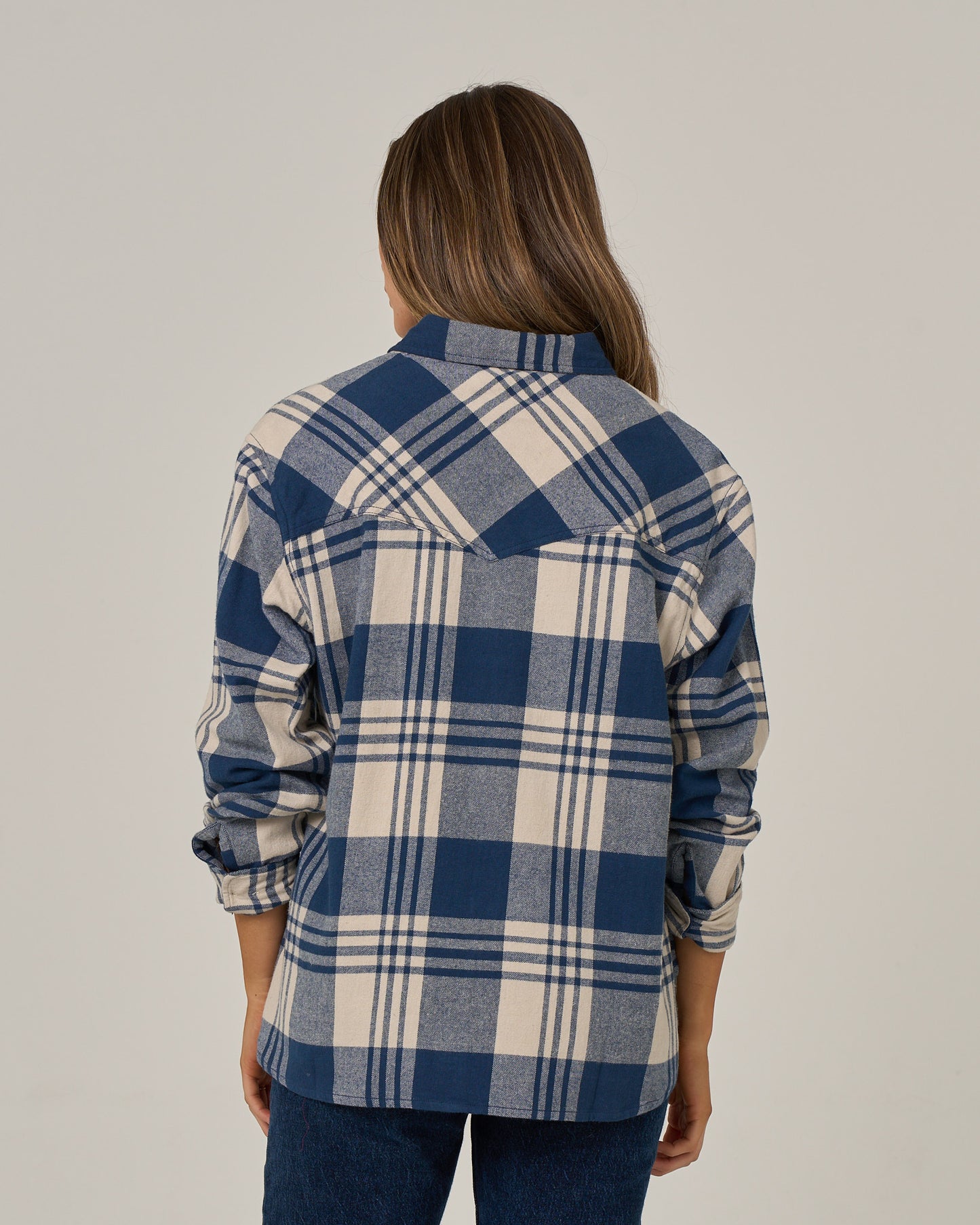 A person with long brown hair, seen from behind, wears the Salty Crew Out West Flannel in navy and blue jeans against a plain, light background.