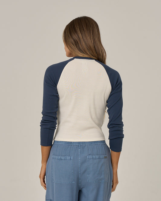 A woman with long brown hair, seen from the back, stands against a plain light background wearing the Salty Crew Truck Bed Long Sleeve - True Navy shirt and blue pants with pockets.