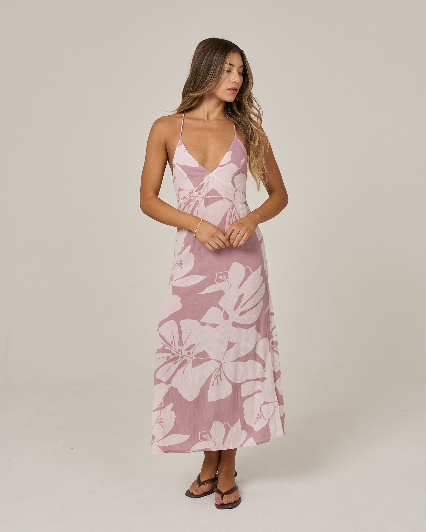A woman wearing the Salty Crew Graphic Bloom Dress in dark navy—a sleeveless viscose slip dress with thin cross-back straps—stands against a plain background, gazing to the side.