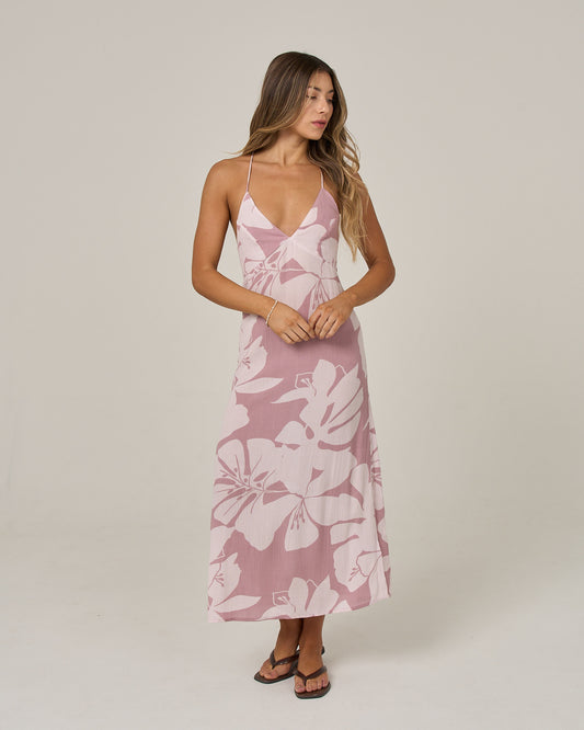 A woman wearing the Salty Crew Graphic Bloom Dress in dark navy—a sleeveless viscose slip dress with thin cross-back straps—stands against a plain background, gazing to the side.