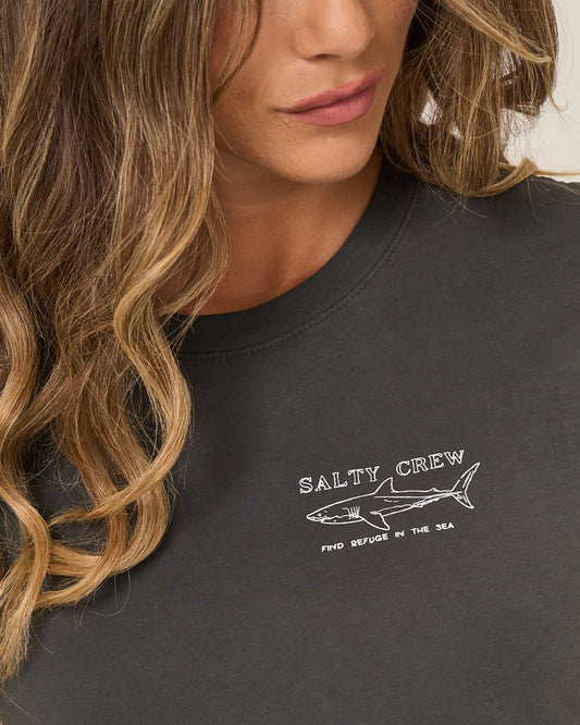 A woman with wavy, light brown hair wears the Salty Crew Shark Anatomy Modern Tee in charcoal, a fitted cotton jersey with cap sleeves featuring a white shark line drawing and "Find Refuge in the Sea.