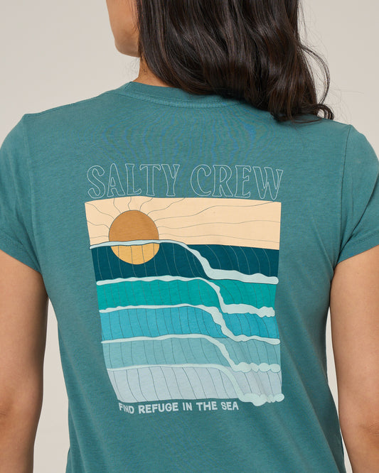 Someone is wearing the Salty Crew Retro Wave Modern Tee in teal, a cotton jersey with cap sleeves, featuring a sun over stylized waves. “SALTY CREW” appears above the print and “FIND REFUGE IN THE SEA” is written below.