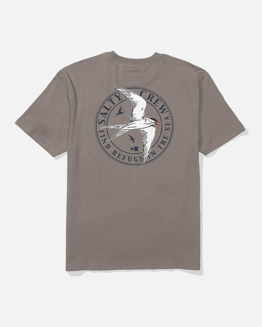 The Salty Crew Tern Original Tee - Cinder is a soft gray cotton t-shirt featuring a screenprinted graphic of a white bird flying over the ocean, surrounded by the words “SALTY CREW” and “FIND REFUGE IN THE SEA,” with two smaller birds accenting the design.