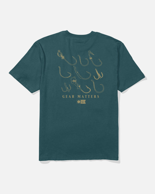 The Salty Crew Fish Gear Original Tee in Atlantic Blue features a soft spun, 100% cotton construction for ultimate comfort. The back is screenprinted with various fishing hook illustrations and the words “GEAR MATTERS” in beige.