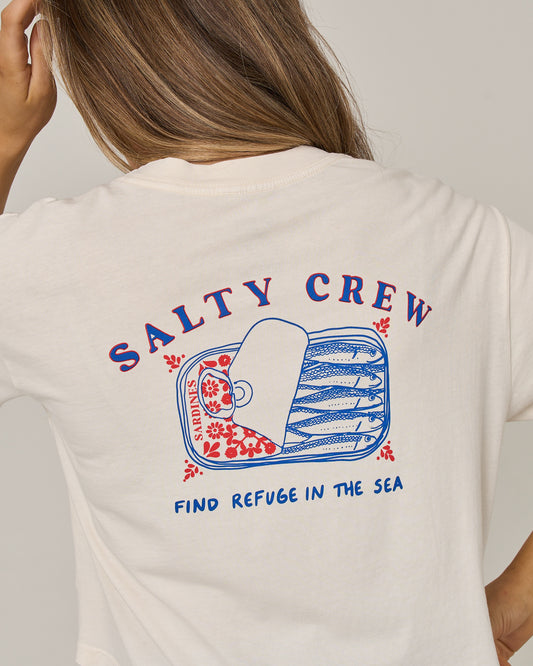 A person wearing the Salty Crew Cute Tin Skimmer Tee in off white, featuring a graphic of an open sardine can with red and blue fish inside and the text “Salty Crew” and “Find Refuge in the Sea.”.