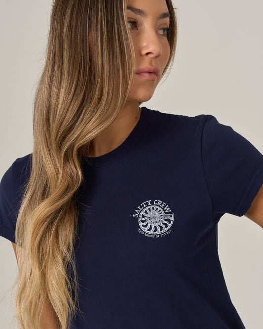 A woman with long wavy blonde hair wears the Salty Crew Nautilus Modern Tee in Bright Navy, featuring cap sleeves, as she looks to the side against a plain background.