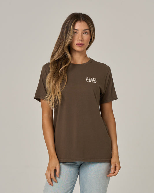 A woman with long, wavy hair wears the Salty Crew Lobster Roll Boyfriend Tee in washed brown and light blue jeans, standing against a plain, light background.
