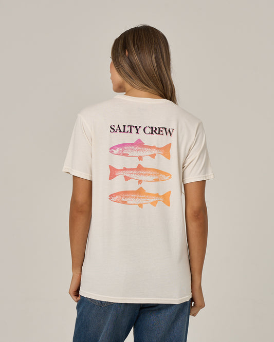 A person with long hair, facing away from the camera and wearing blue jeans, is dressed in the Salty Crew Daily Catch Boyfriend Tee in off white—a relaxed fit cotton jersey tee featuring three colorful fish graphics and Salty Crew branding on the back.