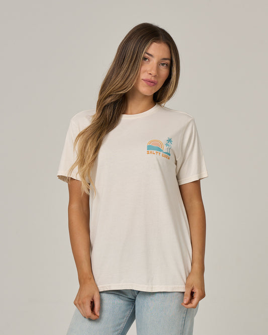 A woman wearing the Salty Crew Sushi Roll Boyfriend Tee in Off White—featuring a relaxed fit, short sleeves, and a small graphic with a rainbow and palm tree above the Salty Crew logo on the chest—stands against a plain background. This cotton jersey t-shirt offers effortless style and comfort for any casual look.