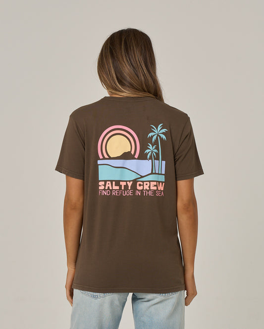 A person is seen from behind wearing the Salty Crew Sushi Roll Boyfriend Tee in washed brown, a relaxed fit short sleeve crafted from soft cotton jersey. The tee features a graphic of a sunset, waves, and palm trees along with the text “SALTY CREW FIND REFUGE IN THE SEA.”.