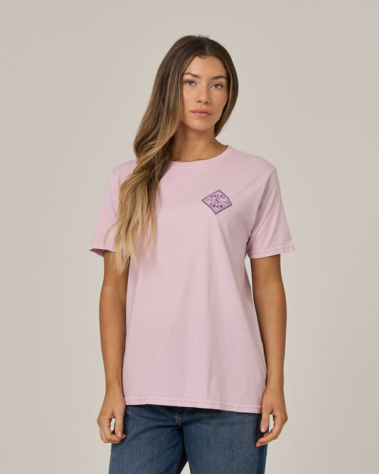 A woman with long, wavy hair wears the Salty Crew Tippet Fill Boyfriend Tee in Pale Orchid—a relaxed fit, light pink cotton jersey shirt featuring a small purple graphic screen print on the left chest. She stands against a plain, light background.