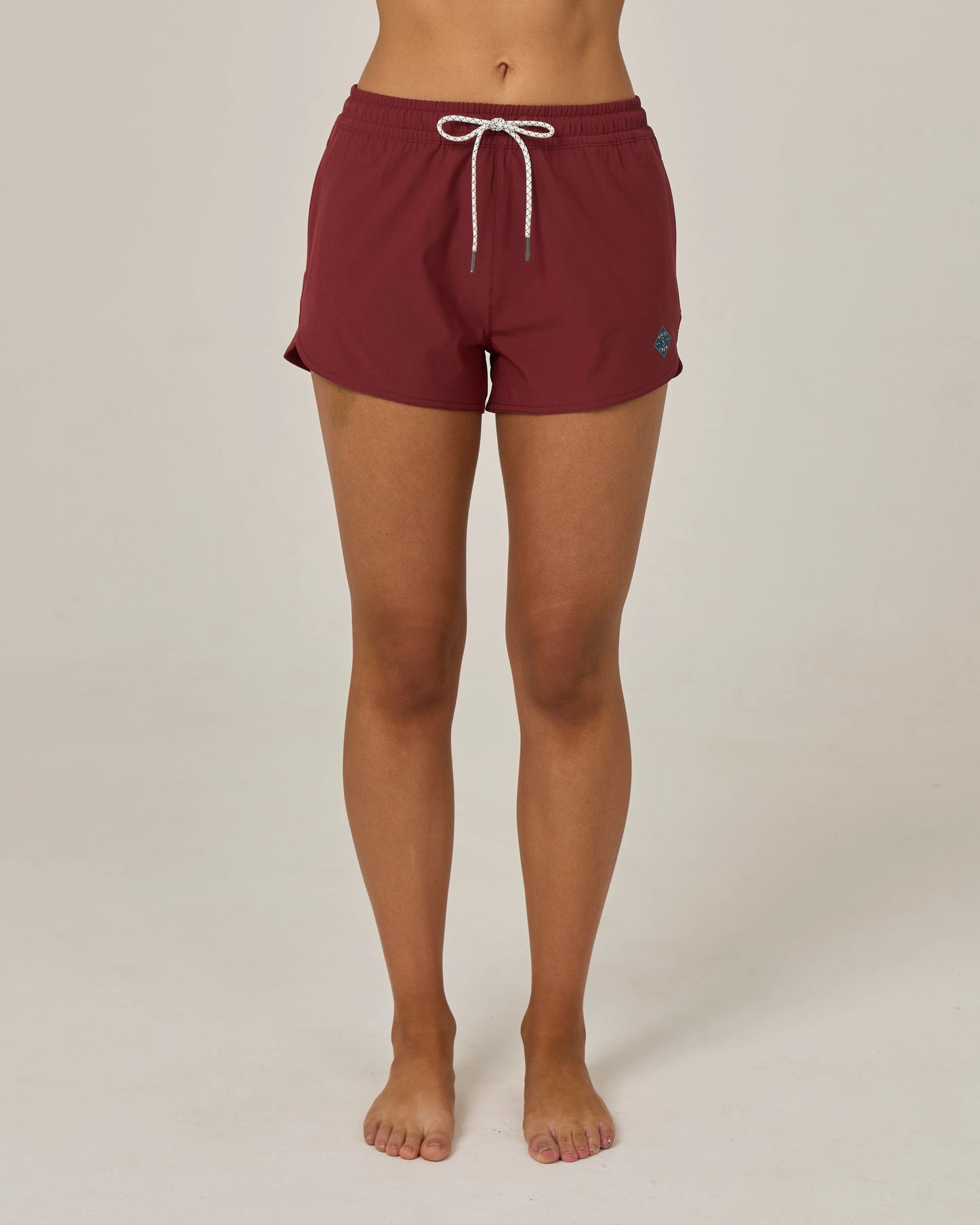 A person barefoot, shown from the waist down against a plain light background, wearing the Salty Crew Beacons Short in maroon with a white drawstring and scalloped hem.