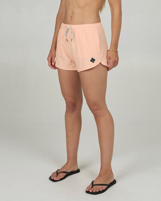 A person wearing Salty Crew Beacons Short in Melon, a simple gold bracelet, and black flip-flops stands against a plain light gray background. The image is cropped from the shoulders down.