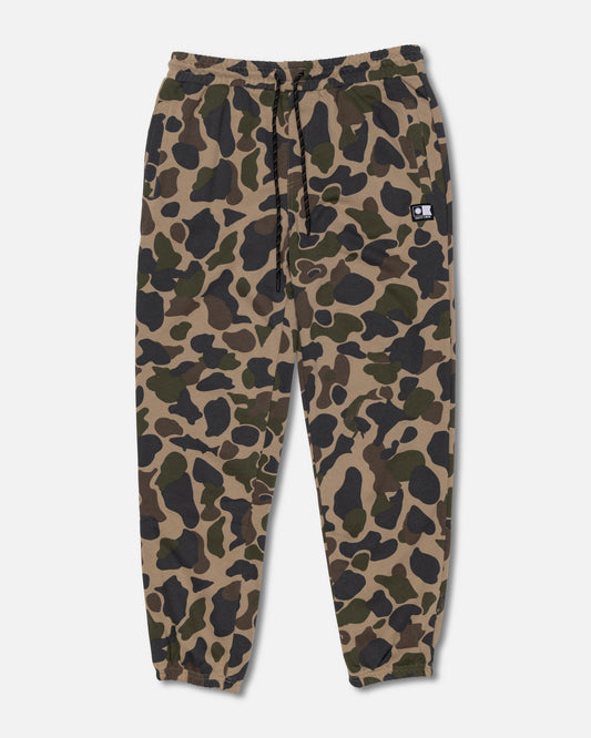 The Salty Crew Crewser Fleece Pant in Sand Camo features an elastic waistband with a drawstring, elastic cuffs, convenient side hand pockets, and a small black patch on one front pocket. The pants showcase a green, brown, and black camouflage pattern.