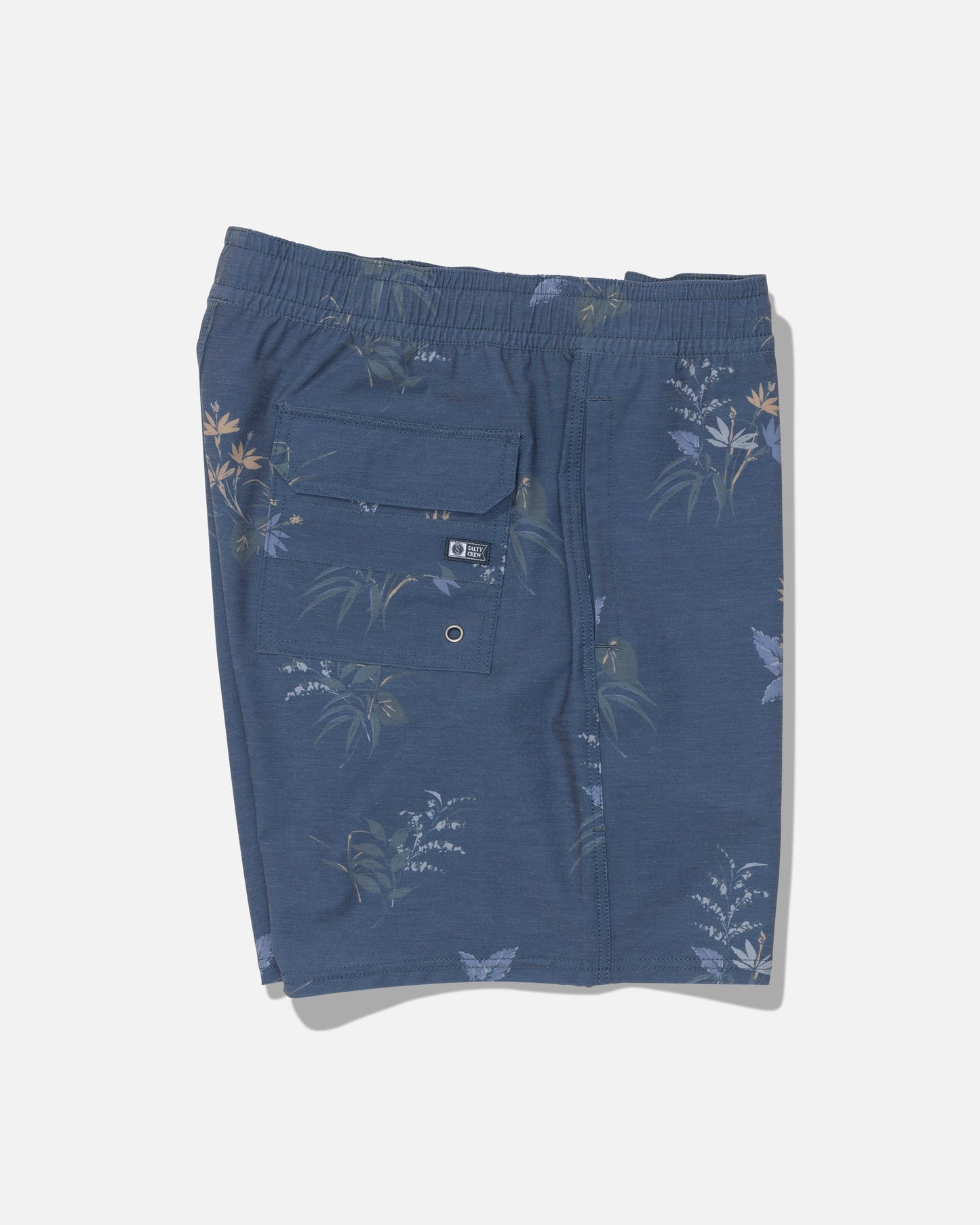 Salty Crew Crew Volley 17″ shorts in Mid Blue featuring a floral print, straight leg cut, and elastic waistband. Includes a back pocket with button flap and a small round metal ventilation grommet. Crafted from recycled polyester with 4-way stretch for comfort and flexibility. Shorts are shown laid flat against a white background.