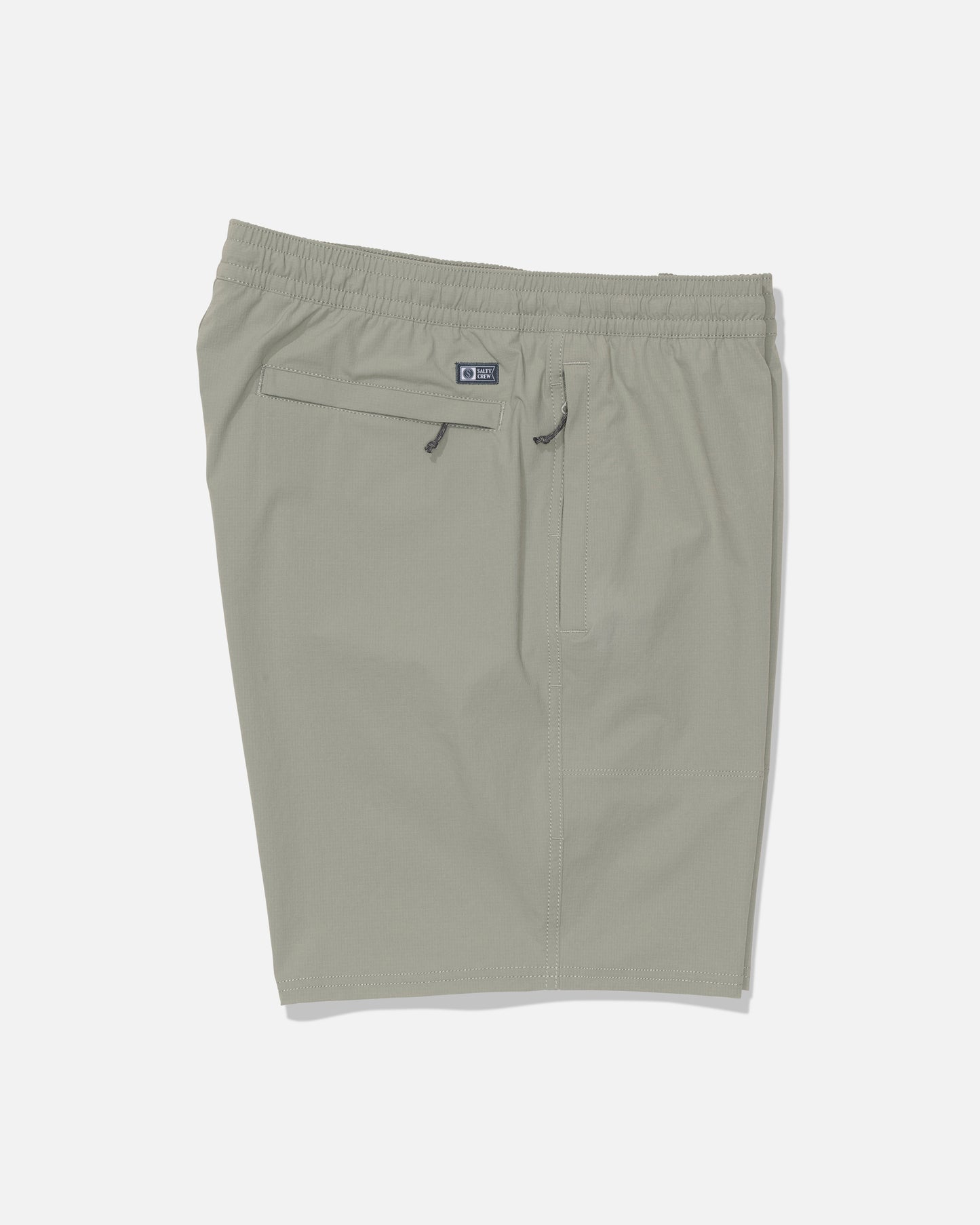 Salty Crew’s Crew 18″ Ewaist Boatshort in Aqua Grey, shown laid flat on a white background, is made from quick-dry ripstop fabric with 4-way stretch for maximum comfort. These light gray athletic shorts feature an elastic waistband, a zipper back pocket, and a subtle Salty Crew logo patch above the pocket.