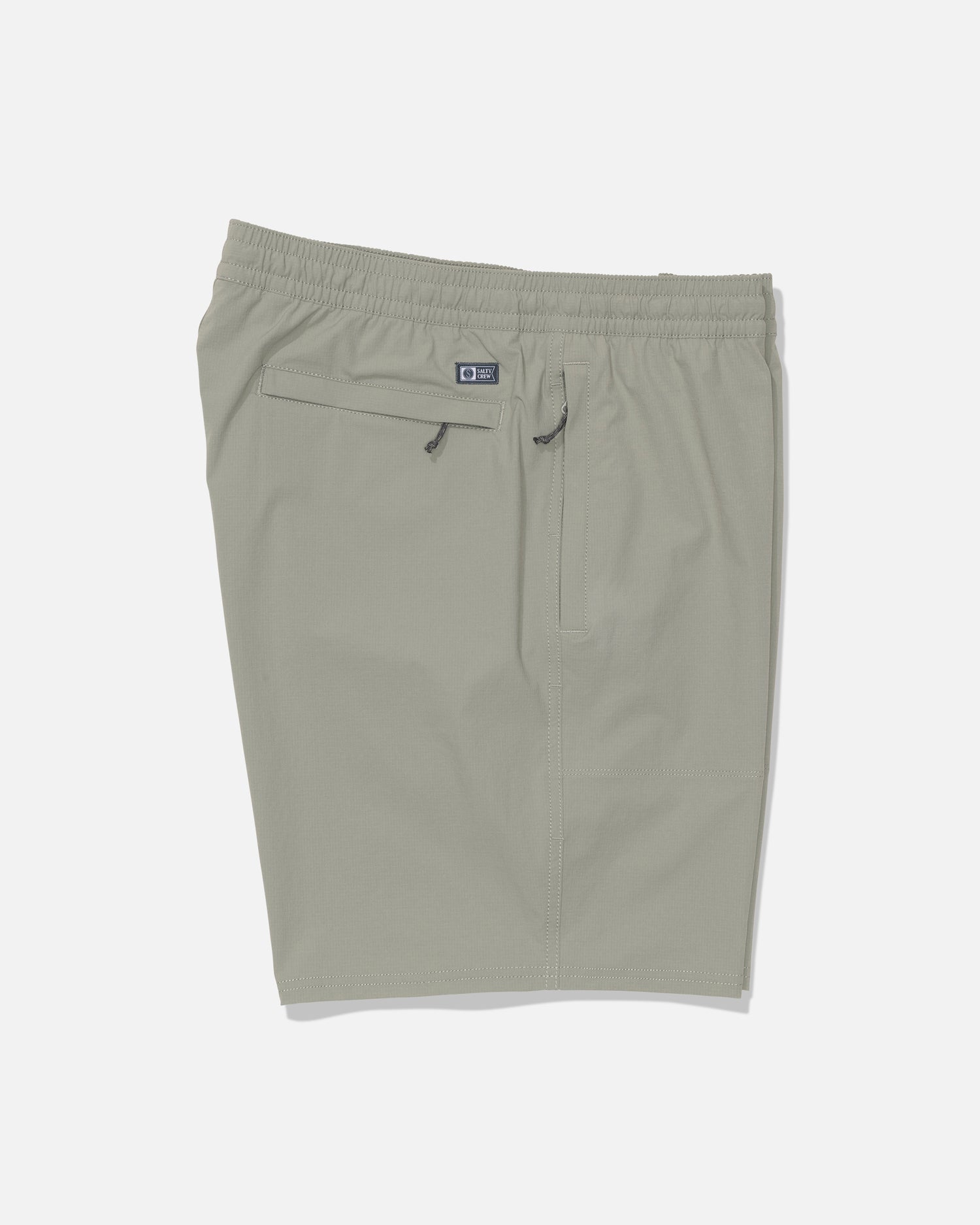 Salty Crew’s Crew 18″ Ewaist Boatshort in Aqua Grey, shown laid flat on a white background, is made from quick-dry ripstop fabric with 4-way stretch for maximum comfort. These light gray athletic shorts feature an elastic waistband, a zipper back pocket, and a subtle Salty Crew logo patch above the pocket.