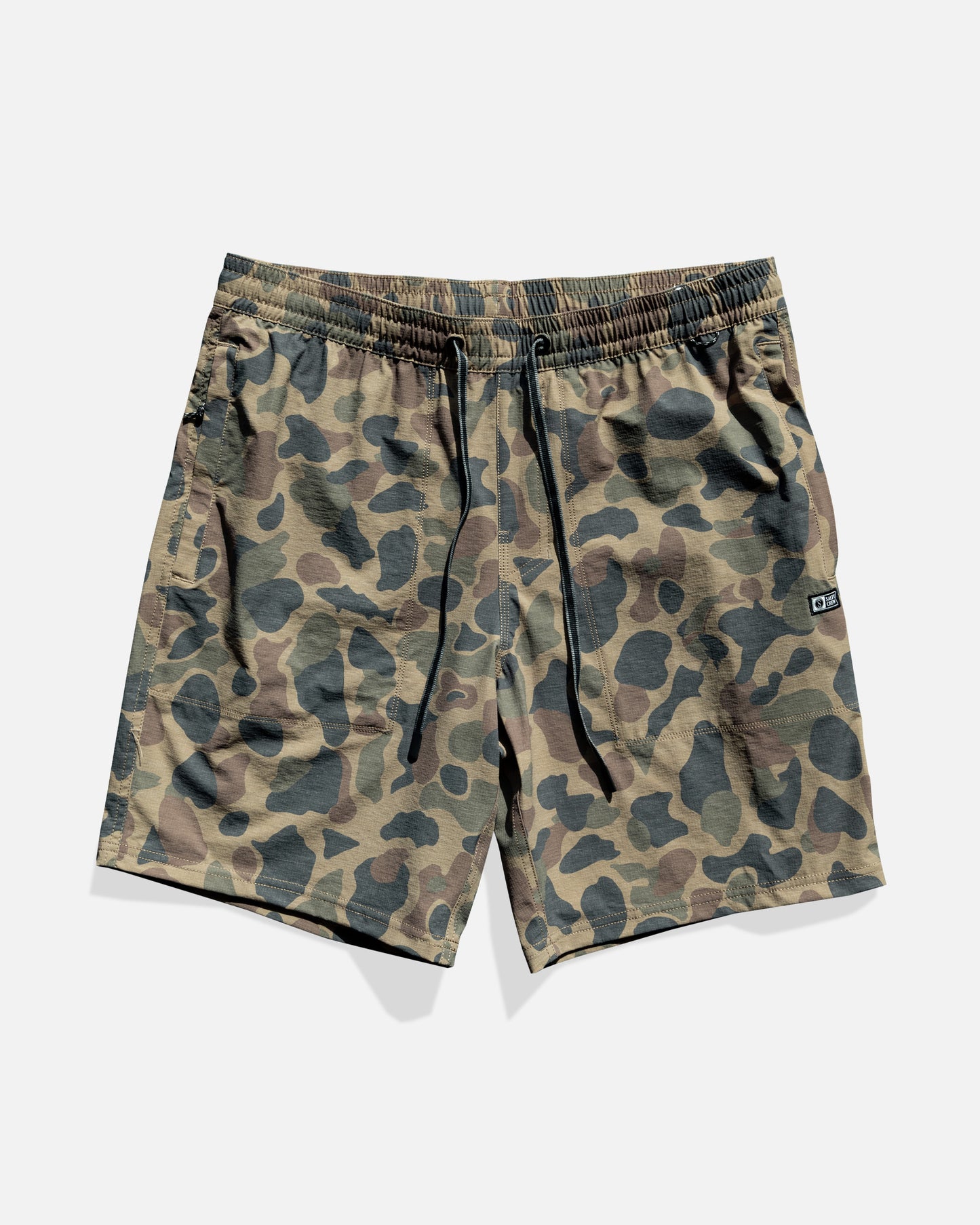 The Salty Crew Crew 18" Boatshort Ewaist in Sand Camo features green and brown camo, elastic waistband with black drawstrings, a logo patch on the left leg, and is made from quick-dry ripstop fabric. Shorts are shown flat on a white background.