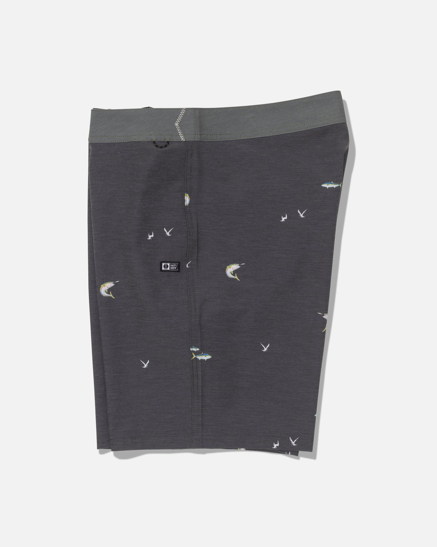 Salty Crew’s Crew 19″ Boardshort in dark grey features a green-gray waistband and is made from recycled polyester, offering comfortable 4-way stretch. The boardshort displays a subtle fishing motif with small fish and bird illustrations, shown against a plain white background.