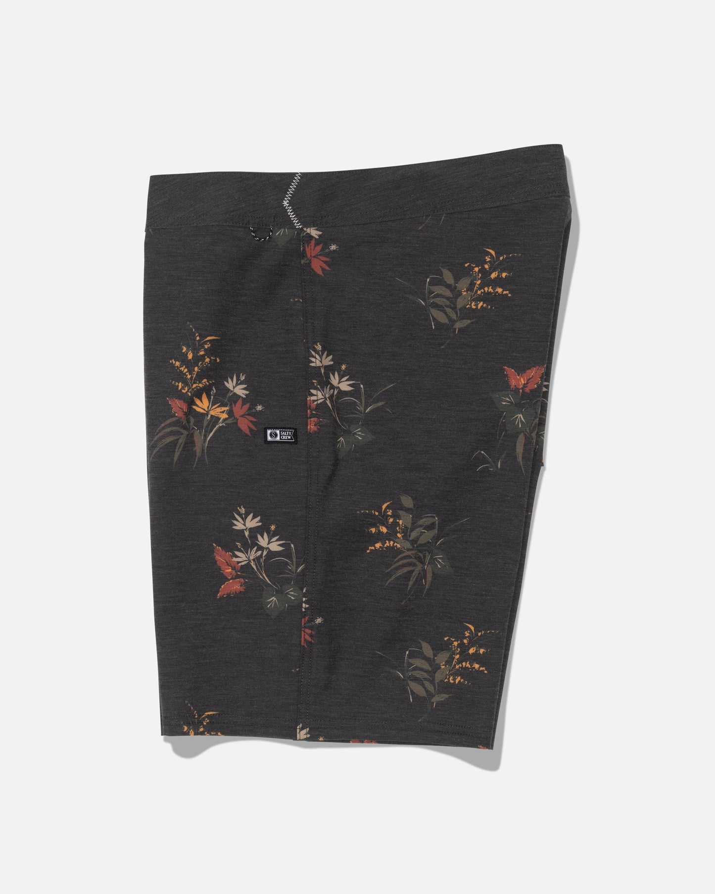 The Crew 19″ Boardshort - Off Black by Salty Crew is crafted from recycled polyester with 4-way stretch for optimal movement. These dark gray boardshorts feature a subtle floral pattern with red, orange, and yellow flowers, along with green leaves. Displayed flat against a white background, they include a small black logo patch on the left side.
